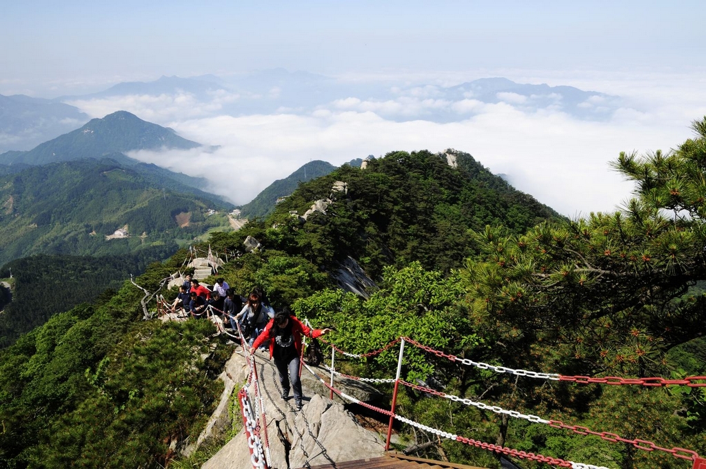 Bodaofeng: walkers on a narrow rocky ridge above green forest and clouds